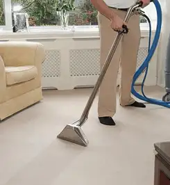 Professional carpet cleaner using a hot-water extraction wand and hose machine in a living room in Arvada, CO.