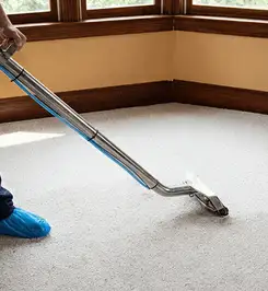 Steam carpet cleaning technician using a hot-water extraction wand on a residential carpet, wearing blue protective shoe covers Arvada, CO.