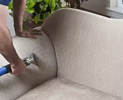 Professional upholstery cleaner deep-cleaning a fabric sofa with a handheld extraction tool and hose in Arvada, CO.